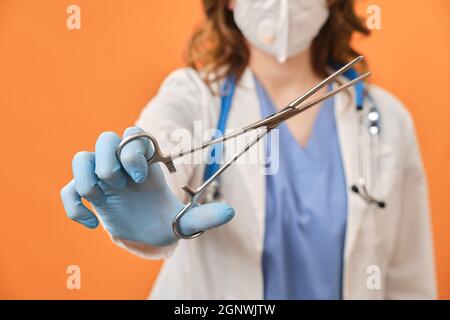 The doctor holds a surgical clamp in his hand. Nurse with a medical clip with scissors in her hand, studio background Stock Photo