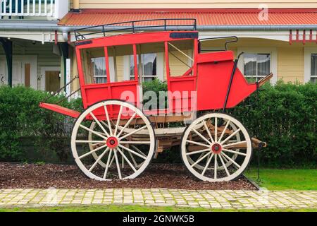 A bright red replica of a western-style stagecoach, with historic buildings in the background Stock Photo