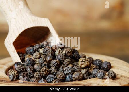 Closeup of dry black pepper corn in a bowl with a scoop. Dried black pepper corn n a wooden bowl on wooden background. Stock Photo