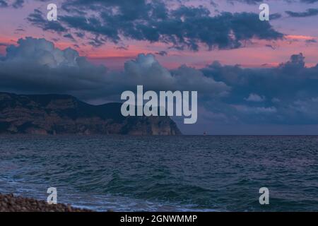 Purple sunset on the sea with clouds, a ship. A beautiful landscape with mountains a lilac sea background. Panorama of the seascape. A ship in the dis Stock Photo