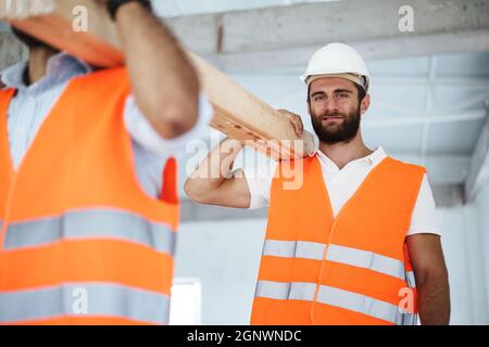 Two young men builders carrying wood planks on construction site, close up Stock Photo