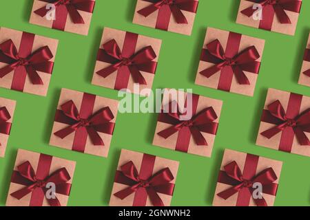 Repetitive pattern made of gift boxes tied with red ribbons on a green background. Holidays concept. Stock Photo