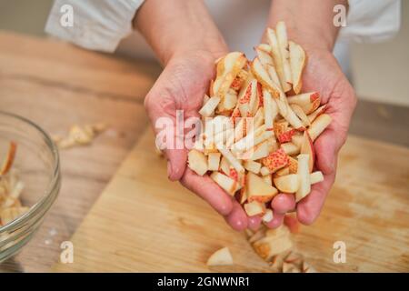 Hands hold sliced apples in handfuls. Adult woman cook a pie on the kitchen table Stock Photo