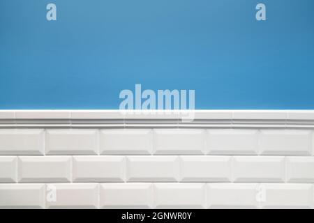 The wall is split horizontally on two zones. The upper part is painted in blue, the lower one is tiled with white hog tiles. Ceramic frieze. Bathroom Stock Photo