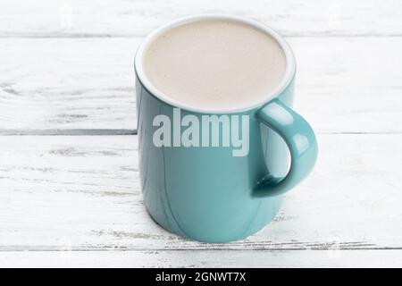 Cup of cappuccino coffee in a blue mug on white wooden background. Stock Photo