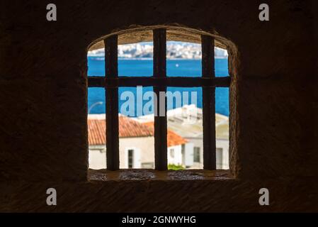 View from the dark prison cell of a window with wrought iron grating (Castle grill) and view to blue sea of an ancient castle Stock Photo