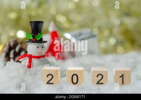 Happy New Year 2021 creative ideas at cubes on snow and background snowman and Christmas tree. Stock Photo