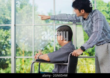 Asian senior disabled businessman in wheelchair discuss interacting together with the team in the office. The old man in a wheelchair and his young so Stock Photo