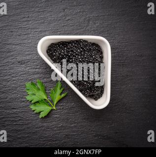 black grainy caviar of paddlefish fish in a white ceramic bowl, black background, top view Stock Photo