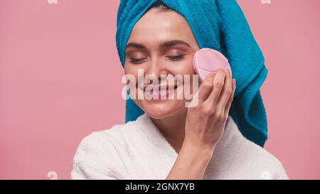 joyful woman using silicone facial cleanser with closed eyes isolated on pink Stock Photo