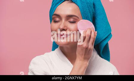 pleased woman with closed eyes using silicone facial cleansing brush isolated on pink Stock Photo