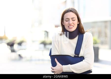 Front view portrait of a stressed woman suffering with broken arm on a sling walking in the street Stock Photo
