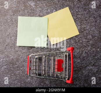 Above blank paper stick note list yellow and green with the shopping cart on concrete background, Shopping reminder concept Stock Photo