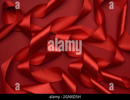 curled red silk ribbon on a red background, festive background Stock Photo