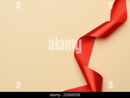 curled red silk ribbon on a beige background, copy space Stock Photo