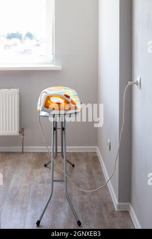 The electric iron is plugged into the socket on the ironing board in the room against the background of the window. Iron clothes. Stock Photo