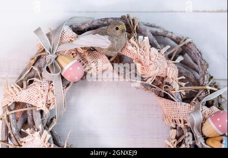 Handmade Easter wreath made of twigs and ribbons with cute bird and wooden eggs. Stock Photo