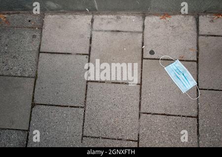 A light blue mouth and nose mask lying on the pavement. Stock Photo