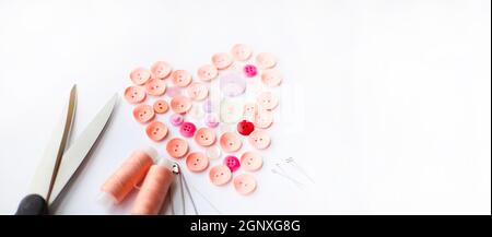 Heart-shaped pink assorted buttons. Scissors and pink spools of thread. Sewing pins and needles. Sewing hobby. Sew to order. Sewing business. Stock Photo