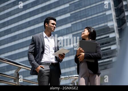 Handsome young Indian businessman in corporate wear talking with businesswoman outdoors in the city Stock Photo