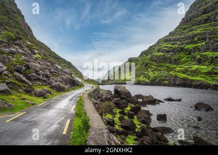 Narrow winding road running alongside lake and stream in green valley, Gap of Dunloe in Black Valley, Ring of Kerry, County Kerry, Ireland Stock Photo