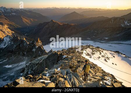 Woman stands alone on the peak of rock. Hiker watching to autumn Sun at horizon . Beautiful moment the miracle of nature. Colorful mist in valley. Stock Photo
