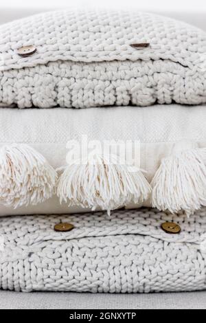 A pile of white and beige knitted sofa pillows with buttons and cotton tassels. Cozy textile textures, interior hygge and home handmade design concept Stock Photo