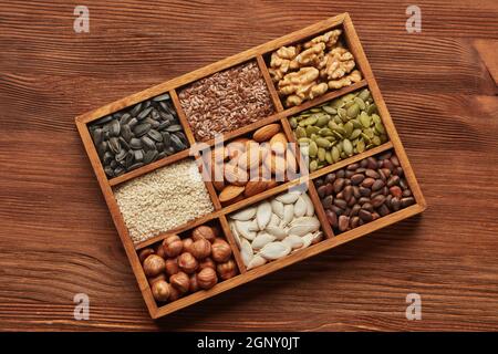 Various varieties of nuts dried seeds lying in wooden box on brown wooden background. Top view. Healthy food. Vegetarian nutrition Stock Photo
