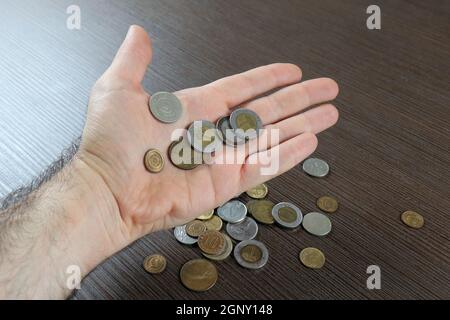 Male hand holding several international currencies coins with more on wooden background Stock Photo