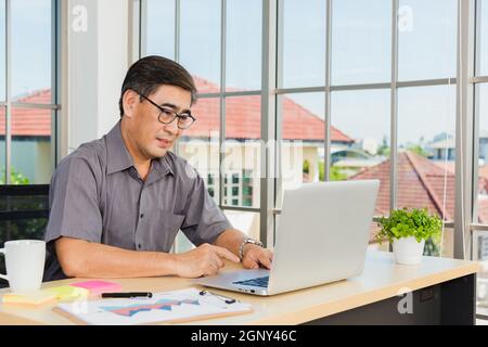 Asian senior business man working online on a modern laptop computer he looking at the screen for remote online studying. Old businessman people using Stock Photo