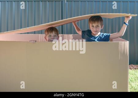 Kids sitting inside a big carton box on the backyard on a day Stock Photo