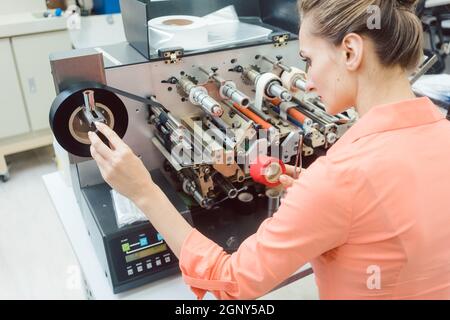Diligent worker woman putting new labels in printing machine Stock Photo