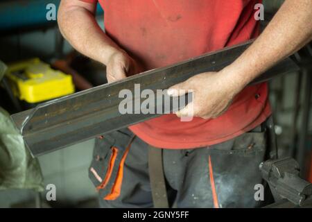 Worker with metal. The guy holds a steel part. Hard work in a metalworking workshop. Creation of steel construction. The working hands of a man. Stock Photo
