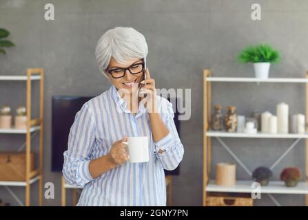 Happy senior woman holding a cup of coffee, talking on her cellphone and smiling Stock Photo