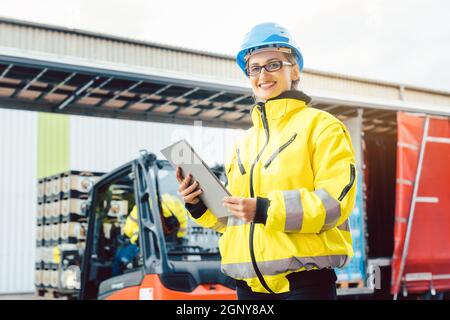 Supervisor checking contents of shipment to be sent by truck on her tablet computer Stock Photo