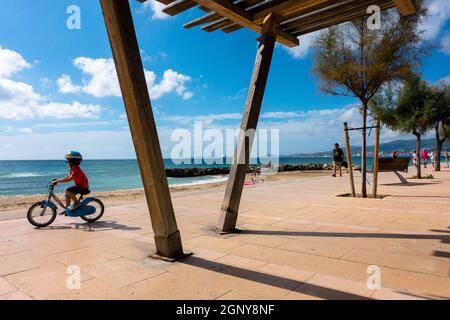 A child riding a bike on a cycle path at sea promenade Paseo Maritimo El Molinar, Palma de Mallorca Spain paved public walk along seafront toddler Stock Photo