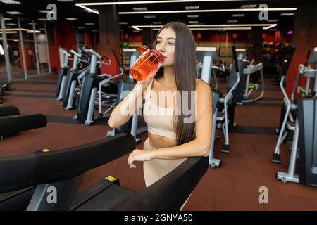 Girl drinks water from a shaker after exercising on a treadmill Stock Photo
