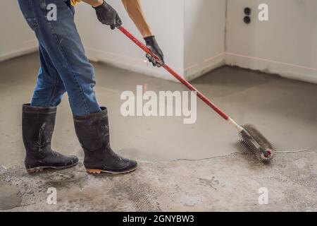 plasterer during floor covering works with self-levelling cement mortar, uses a needle roller Stock Photo