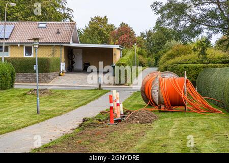 There is more progress in Tullebølle than the name suggests: fiber optic cables are being laid to every house in this sleepy village on Langeland, Denmark. A cable drum with orange conduit lies in front of a carport. Stock Photo