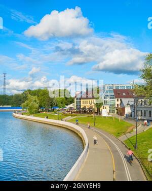 MINSK, BELARUS - JULY 17, 2019: People walking and cycling by Svisloch river embankment in bright sunny daytime, green park and city architecture in b Stock Photo