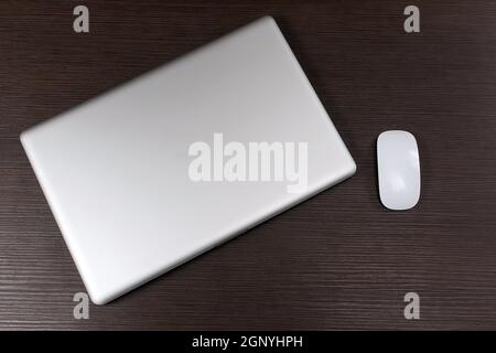 Modern closed laptop computer with wireless mouse on wooden table Stock Photo