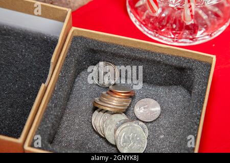Empty, unwrapped gift box filled with pennies, nickels, dimes, quarters, and a dollar coin, on a red table top Stock Photo