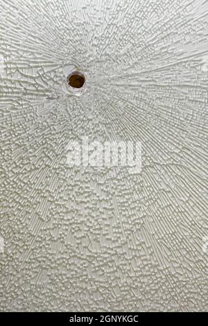 Broken tempered glass with white backing, cracks around the hole Stock Photo