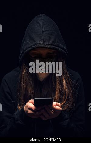 Hooded cyber crime hacker using mobile phone internet hacking in to cyberspace,online personal data security concept. Stock Photo