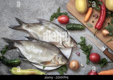 On the plate are two large bream. Nearby are vegetables and spices for cooking this river fish. Top view with copy space. Flat lay Stock Photo