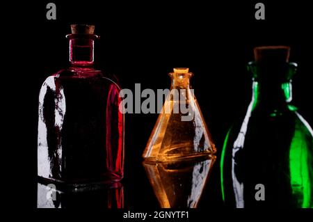 Still life of three colored decorative bottles with corks on glass against black background. Stock Photo
