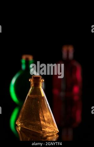 Still life of three colored delpratoven bottles with corks on glass against black background. Stock Photo