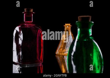 Still life of three colored decorative bottles with corks on glass against black background. Stock Photo