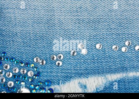 Light-blue torn denim with blue and silver rhinestones, background. Top view Stock Photo