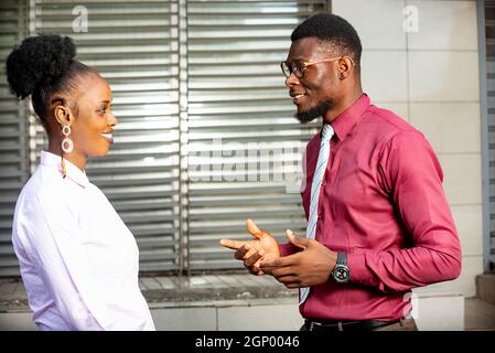 businessman and businesswoman standing and talking together near the office of the business center smiling Stock Photo